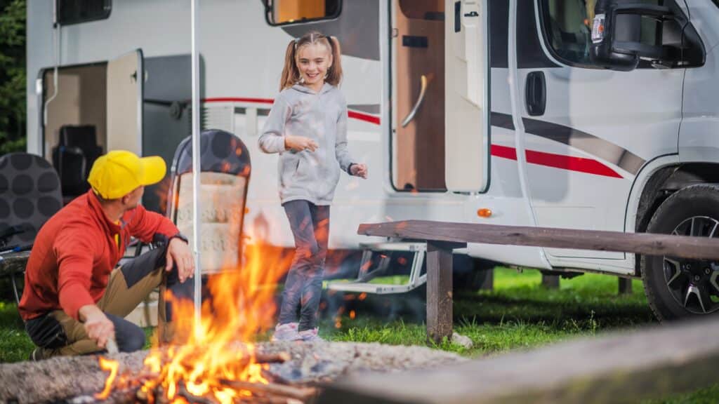 Family RV Road Trip Campsite. Caucasian Family. Father with Daughter Having Fun in Front of Campfire. Recreation Vehicle Traveling.